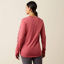 Back view of a person wearing a pink shirt that says Ariat down the sleeve of the arm against a beige background.