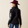 Back view of a person wearing a black jacket with white writing against a beige baackground.