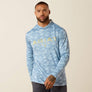 Man wearing a blue camo long sleeve with Ariat in yellow with a beige background