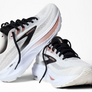 White, black and rose gold running shoes with the brooks logo on a white background