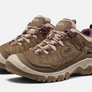 Pair of light brown shoes with tan and dark purple accents that has the Keen logo on the side and tongue of the shoe against a white background.