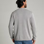 Back view of a person wearing a long sleeve light grey sweater and blue jeans against a medium grey background.