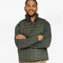 Person wearing a dark green vest with a dark green shirt and khaki pants against a white background.