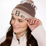 A person wearing a light tan colored winter hat with a pom on the top.