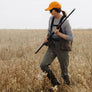 Person in a field holding a rifle wearing olive green pants and a yellow hat