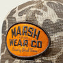 Close up of Marsh Wear Co patch on front of Camo hat with a beige background