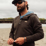 Person wearing a brown 1/4 zip pull over hoodie with nature in the background