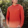 Man wearing an orange long sleeve with a hood and a pocket on front against nature
