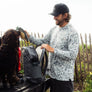 Man wearing a gray camo long sleeve with a hood interacting with a dog with nature in the background