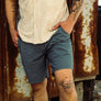 Person wearing a beige shirt and blue shorts standing in front of a rusty metal surface.