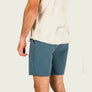 Person wearing blue shorts and a beige shirt on a plain background