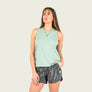 Woman wearing a light green sleeveless top and camouflage shorts on a plain background