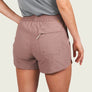 Person wearing dusty brown shorts with a pocket on the back and a grey shirt against a beige background