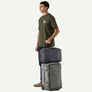 A person holding a suitcase with a second bag on top against a white background.