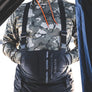 Person wearing camouflage jacket and black suspenders with 'Simms' branding.