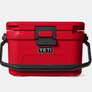 Red cooler with a black handle and a black latch with the Yeti logo on the front against a white background.