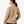 Back view of a person wearing a tan colored sweatshirt against a grey background.