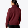 Back view of a person wearing a maroon color long sleeve shirt that has a collar against a grey background.