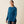 Person wearing a dark blue long sleeve shirt that has Ariat going down the arm in a light blue color and has a pocket on the chest area against a cream colored background.