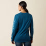 Back view of a person wearing a dark blue shirt with Ariat written in light blue going down the arm of the sleeve.