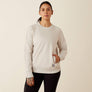 Person wearing a cream color crew neck sweatshirt with her hand in the pocket against a beige background.