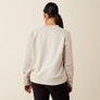 Back view of a person wearing a cream color sweatshirt and black pants against a beige background.