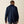 Back view of a man wearing a navy blue shirt and grey pants against a tan background