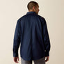 Back view of a man wearing a navy blue shirt and grey pants against a tan background 