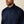 Up close view of a man wearing a navy blue button up collared shirt with a red logo on the front pocket against a tan background