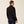 Back view of a person wearing a black jacket against a beige background.