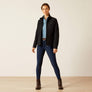 Person wearing a black jacket with blue pants and a light blue shirt against a beige background.