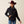 Person wearing a maroon cowboy hat, jeans and a black coat with their hand in the pocket against a beige background.
