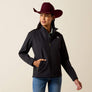 Person wearing a maroon cowboy hat, jeans and a black coat with their hand in the pocket against a beige background.