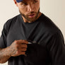Man wearing a dark grey shirt holding out his pocket with a beige background