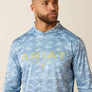 Man wearing a blue camouflage hoodie with 'Ariat' branding on a beige background
