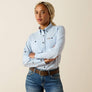 Woman wearing a light blue shirt with black buttons and jeans on a beige background