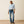 Woman wearing a light blue button-up shirt, jeans, and brown shoes on a beige background
