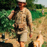 Person wearing a browns trap vest walking in a field with a dog.