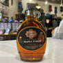 Bottle of maple syrup with a little handle and black cap with the brands logo on the front of the bottle 