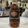 A bottle of maple syrup with a gold cap that has a sticker of the brands logo and maple syrup written on it on the front of the bottle.