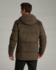 Back view of a person wearing a dark brown jacket with black jeans against a medium grey background.