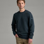 Person wearing a dark blue sweater and khaki pants against a grey background.