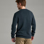 Person wearing a dark blue sweater and khaki pants against a grey background.