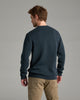 Person wearing a dark blue sweater and khaki pants against a grey background.