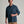 Person wearing a long sleeve dark blue shirt with khaki pants against a grey background.