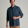 Person wearing a long sleeve dark blue shirt with khaki pants against a grey background.