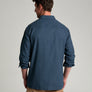 Back view of a person wearing a long sleeve dark blue flannel against a grey background.