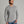 Person wearing a light grey long sleeve sweater with blue jeans against a light medium grey background.