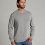 Person wearing a light grey long sleeve sweater with blue jeans against a light medium grey background.
