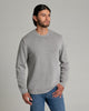 Person wearing a light grey long sleeve sweater with blue jeans against a light medium grey background.